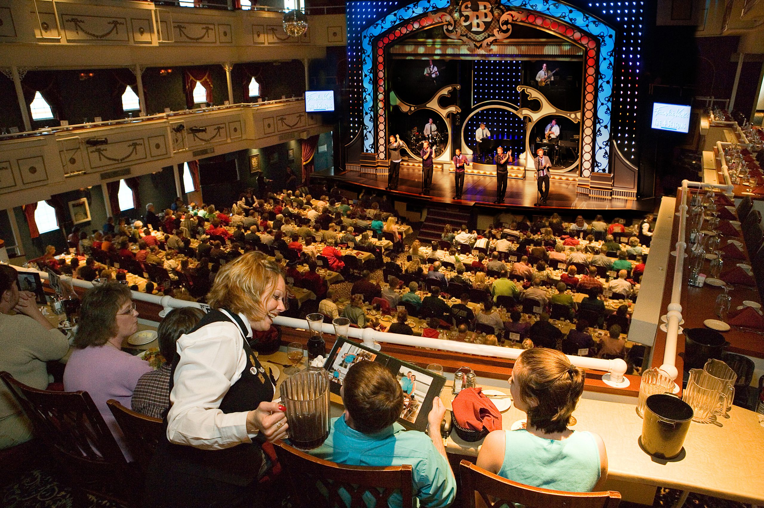 Guests seated at tiered dining tables facing a lit stage where performers sing during a Branson dinner show