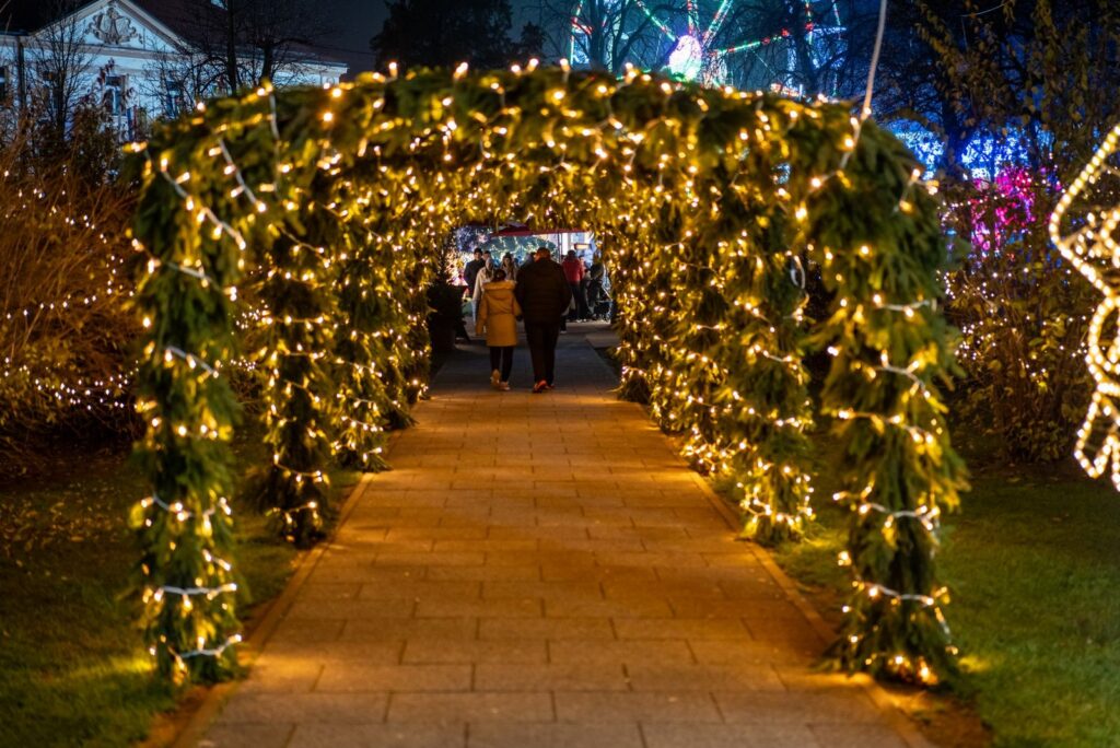 People walking beneath a garland archway strung with warm white lights at dusk