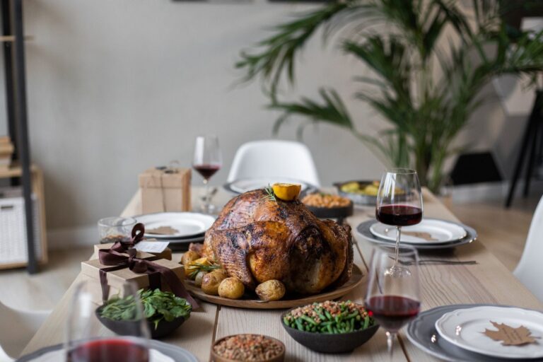 Roast turkey, wine glasses and side dishes laid out on a wooden table for a holiday meal