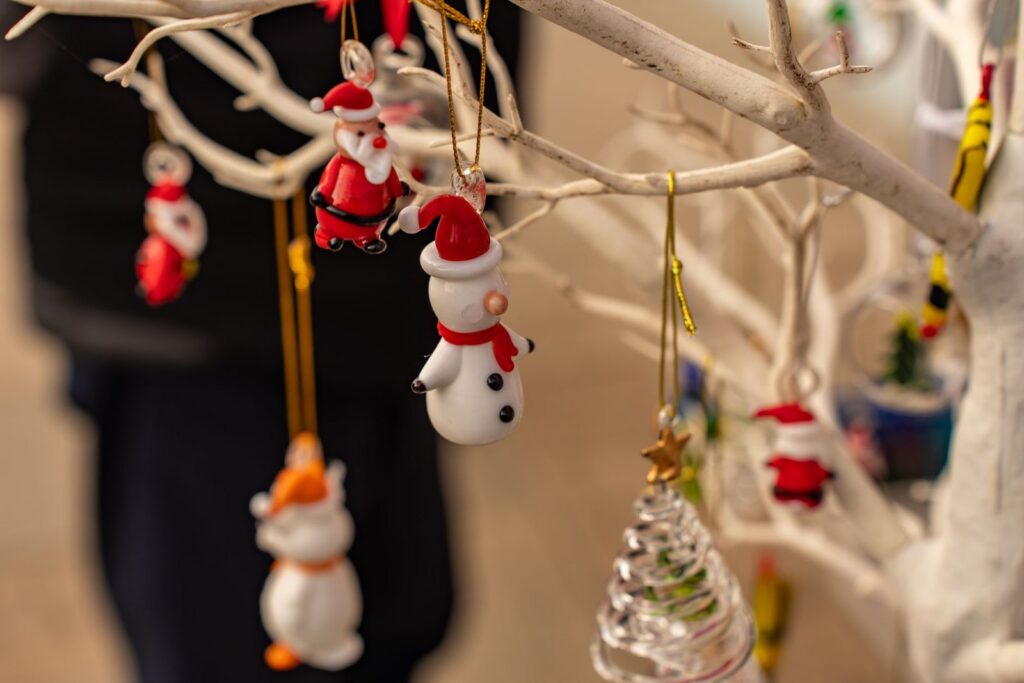 Glass and painted Christmas ornaments including a snowman and a Santa hanging from a white branch
