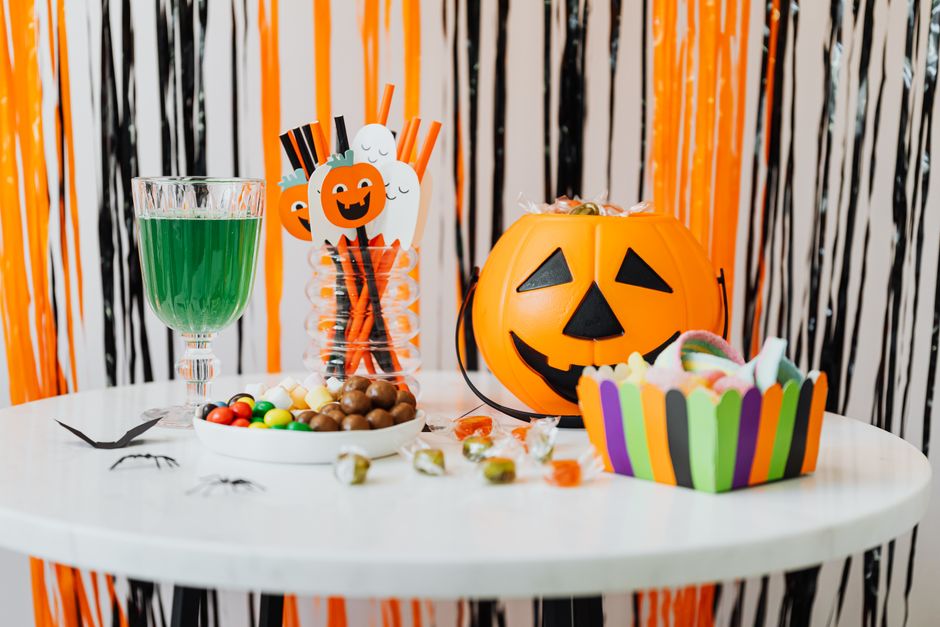 A table set with Halloween candy, a jack-o-lantern bucket and a green drink in front of orange and black streamers