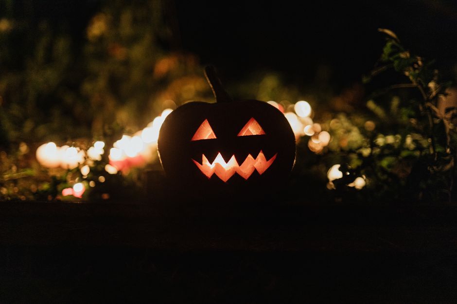 A carved jack-o'-lantern with a jagged grin glowing in front of blurred candle lights