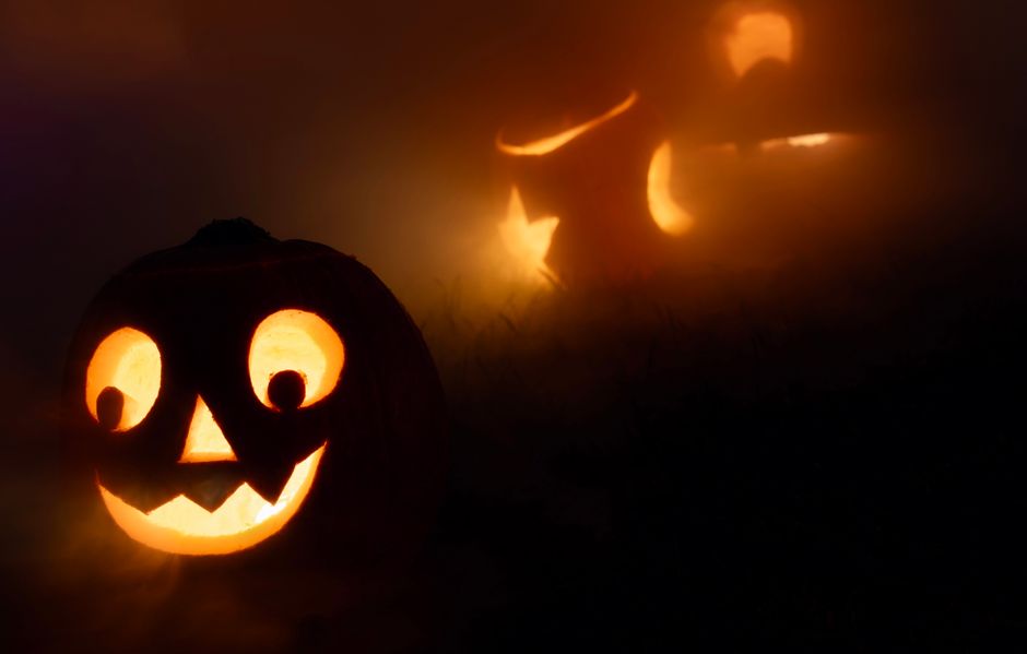 Carved jack-o'-lanterns glowing orange through thick fog at night