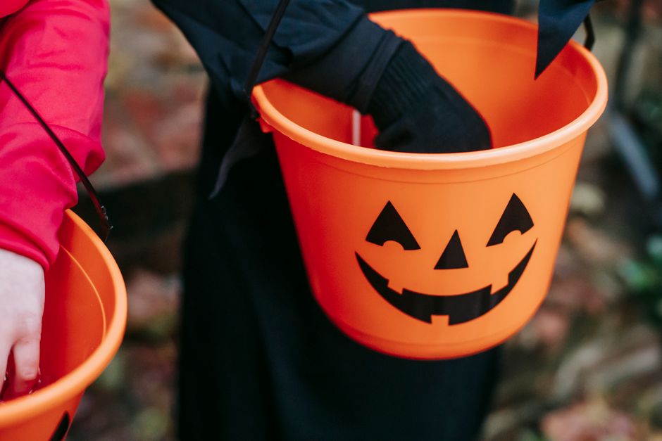 A gloved hand reaching into an orange jack-o-lantern candy bucket